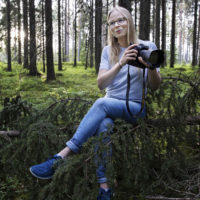 Lina Enlund istuu metsässä kamera kädessä.
